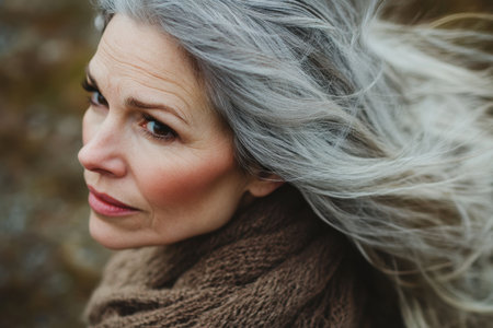 A woman with flowing silver hair looks pensively outdoors, surrounded by nature in soft natural light.の素材
