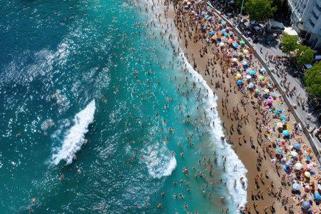 People enjoy a busy beach day under colorful umbrellas by the turquoise ocean water with gentle waves rolling in.の写真素材