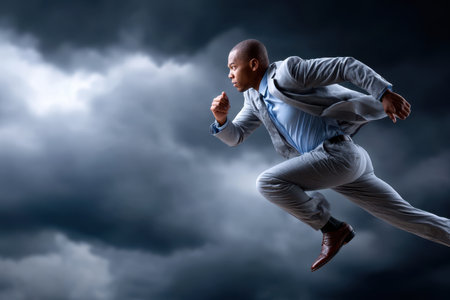 A man dressed in a suit runs with determination beneath a tumultuous, dark sky filled with clouds.の写真素材