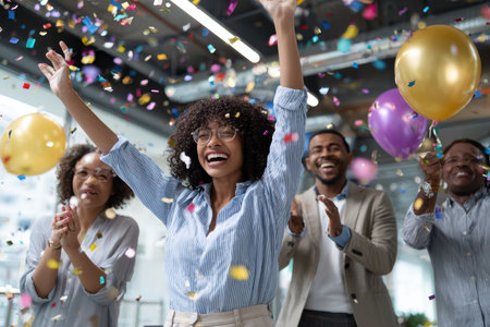 Group of colleagues celebrating together, throwing confetti and enjoying balloons at a workplace party.の写真素材
