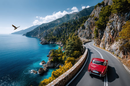 A vintage car on a scenic coastal road, evoking a sense of adventure and nostalgia, in bright, midday light, using a drone camera, with a sudden bird swooping down in front of the car.の素材