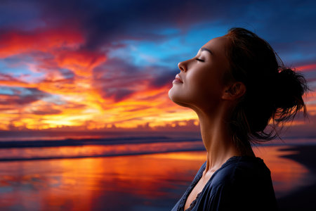 A woman stands quietly on the beach, experiencing a stunning sunset with vibrant colors reflecting on the water.の素材