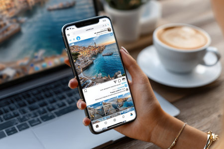 A person admires stunning seaside views on their phone while relaxing with a cup of coffee at a desk.の素材