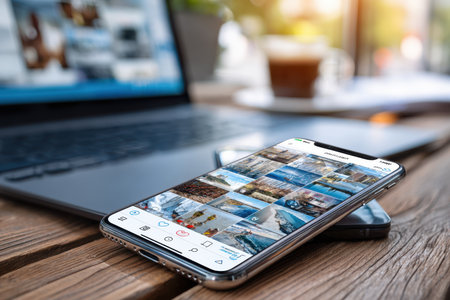 A smartphone shows vibrant travel photos, with a laptop and coffee cup nearby, setting a cozy workspace vibe.の素材