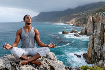 A person practices meditation on a rocky ledge overlooking the ocean, surrounded by beautiful cliffs at dawn.の素材