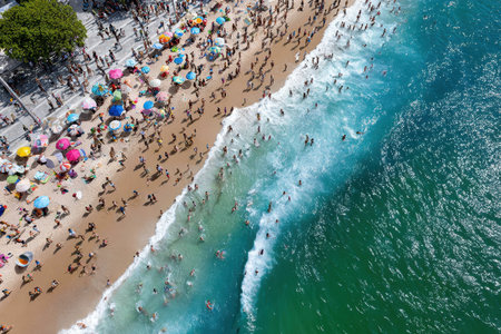 Crowds of people gather at a vibrant beach to swim, sunbathe, and relax under colorful umbrellas.の素材