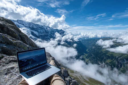 A person works on a laptop sitting on a rock, surrounded by stunning mountains and clouds in Switzerland.の写真素材