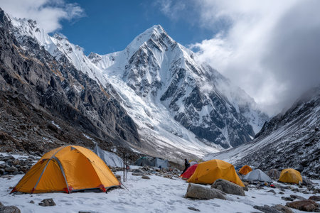 Brightly colored tents are pitched on snowy ground at a mountain base camp, with majestic peaks looming above.の写真素材