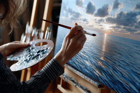 An artist is painting a beautiful sunset reflecting on the ocean water while in a creative workspace.の写真素材