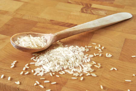 Wooden spoon and rice on chopping boardの写真素材