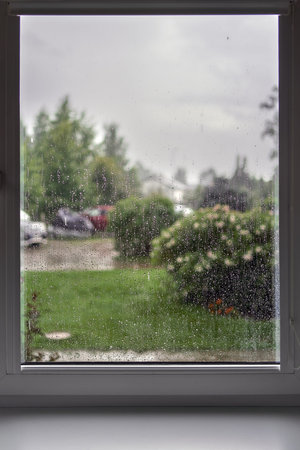 Rainy day view from the window, raindrops on glass, blurred cloudy rainy sky background