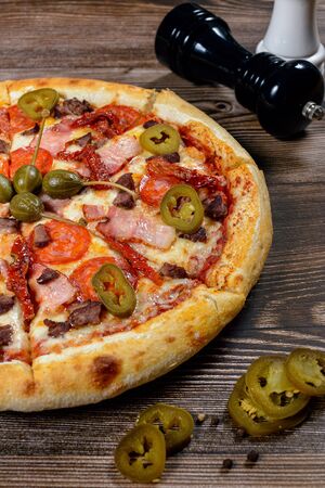 Pizza with jalapeno pepper, capers, bacon and pepperoni on wood backgroundの写真素材