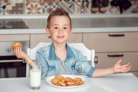 Smiling little boy eating tasty cookies with milkの写真素材