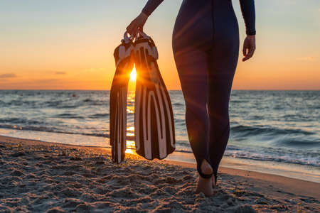A girl diver in a wet suit holds flippers in her hands.の写真素材
