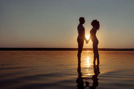 Loving couple stands holding hands in the water. Couple on the sunset.の写真素材