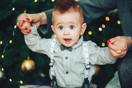 Surprised baby boy wearing a bow tie and shirt against the beautiful bokeh lights of the Christmas...