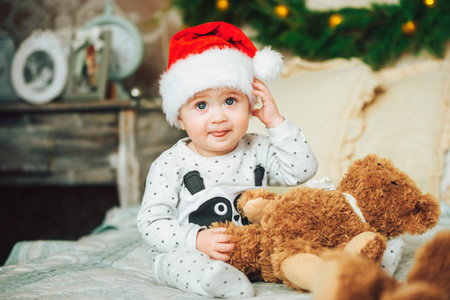 Little child wearing red Christmas cap amusingly shows the tongue. Cheerful caucasian one year old...