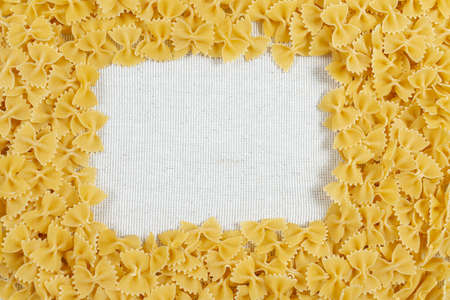 Farfalle pasta making a frame on rustic linen fabric. Flat lay. top view. Copy space for your recipeの写真素材