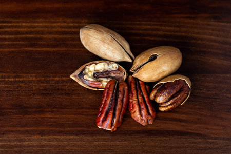 Pecan nuts on a wooden table. Heap or stack of pecan. Cracked and opened pecan nuts and nuts in...