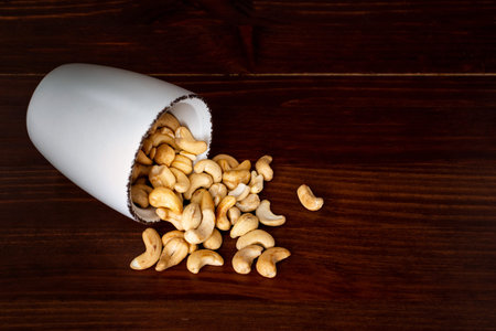 Scattered cashew in a bowl against dark rustic wooden background. Cashew nuts