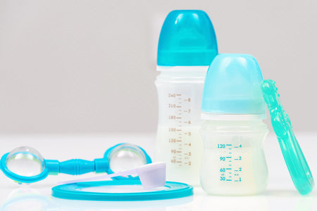 Children's feeding accessories on white table. Baby food concept. Blue bottles with milk, spoon with...