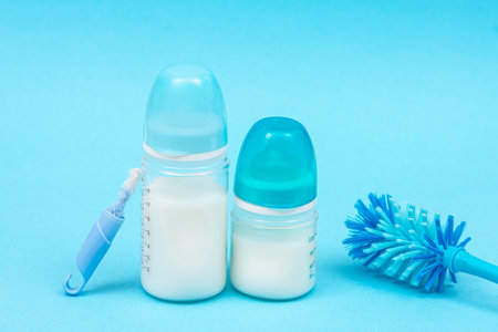 Baby bottles with milk and nipples bottle brush accessories on blue background. Baby products,...