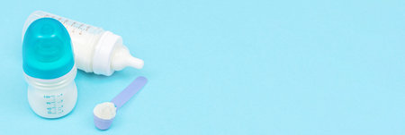 Banner with milk powder for baby in measuring spoon near baby bottles on blue background. Baby...