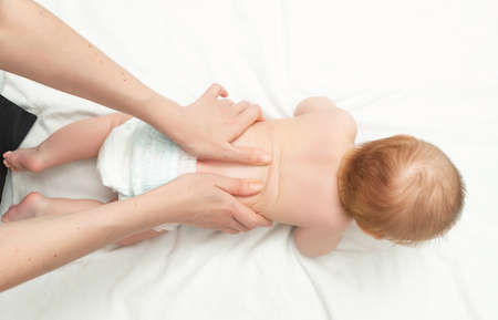 The baby is 5 months old, lying on his tummy. Mom gives back massage to the child, for its development. Childrens gymnastics and exercises. Top viewの写真素材