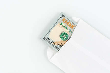 US dollars in a white envelope on a white background. The concept of income, bonuses or bribes. Corruption, salary, bonus. Close-up photo, top view, copy spaceの写真素材