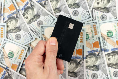 Men's hand holding credit card on money background. Credit card and dollar bills as wealthy concept. Lifestyle, technology, e-commerce, digital banking and online payment conceptの写真素材