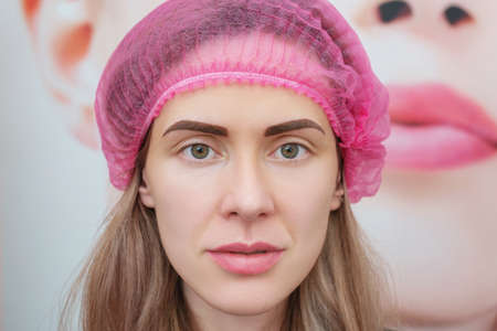 Young woman immediately after permanent eyebrow make-up procedure. Portrait of beauty model after microblading or tattooing of eyebrows. Real peopleの写真素材