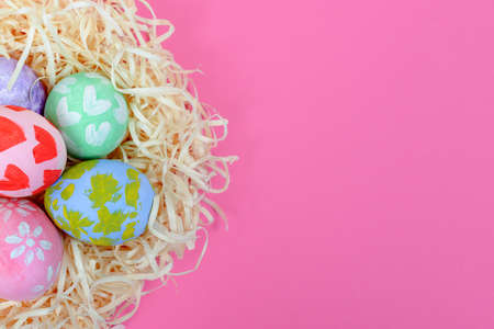 Close up of colorful handmade painted Easter eggs in the nest on a pink background. Eggs painted by a little kid. Top view, space for textの写真素材
