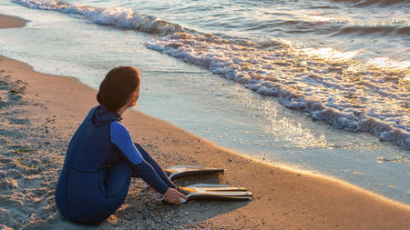 A girl free diver sits on the sea shore puts on her fins and prepares to snorkeling dive. Travel holiday lifestyle concept. Woman opens diving season.の写真素材