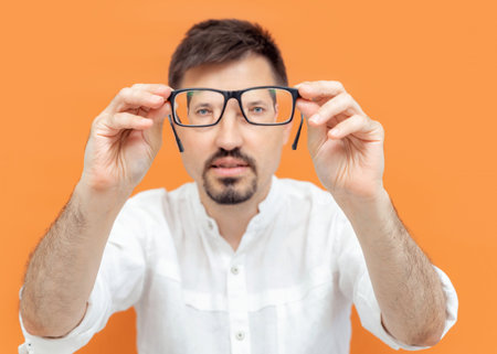 Portrait of thoughtful caucasian man holding eye glasses outstretched and looking through it while...