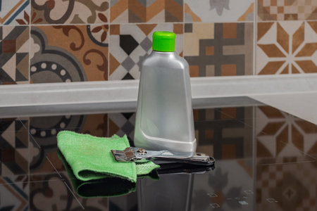 A bottle of hob cleaner, cooker cleaning scraper and a green jay cloth on a cooker in a kitchen....