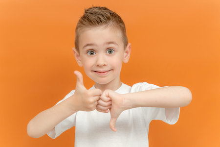 Little Caucasian boy in white T-shirt showing THUMB UP and DOWN gesture in sign language on yellow...