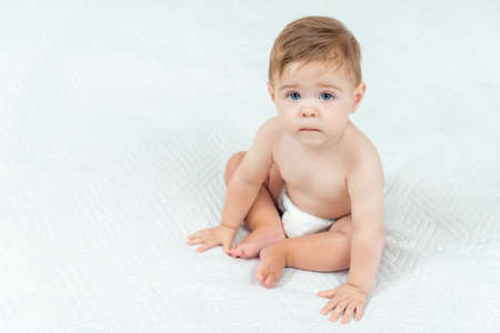 Baby boy in diaper sitting on bed in room. Portrait of cute toddler on white background, copy spaceの写真素材