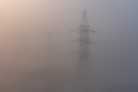 Metal construction of high-voltage power line surrounded by thick fog. Zero visibility. Dark...