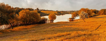 Beautiful rural landscape with meadow and lake. Tranquil autumn evening view over fields with pond in foregroundの写真素材