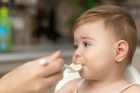 Little Caucasian baby boy with hand close his mouth no eat his food. Kid with dirty messy face sitting in high chair. Feeding time.の写真素材