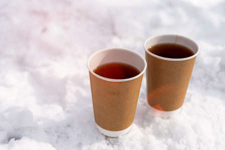Take away craft paper cup with tea against sunlight on the snow in the winter. Street hot drink concept. Copy space.の写真素材