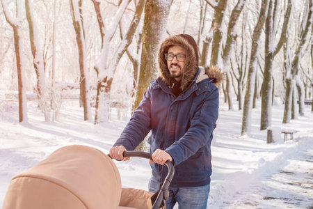 Happy father walks through the park in winter with a baby carriage. Walking with child in winter in the morning. Snowfall, blizzard concept.の写真素材