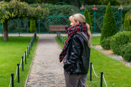 Stylish blond woman in black leather jacket walking in the park. A beautiful fashionable woman....