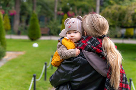 Cute one-year-old child in the arms of his mother. The family walks in the autumn park. A young son is in the arms of his momの写真素材