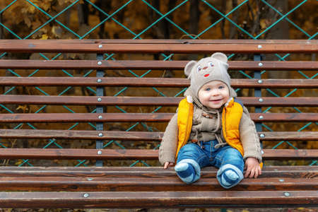 Cute little one-year-old child on a park bench. Portrait of a smiling toddler boy. Walking in the autumn parkの写真素材
