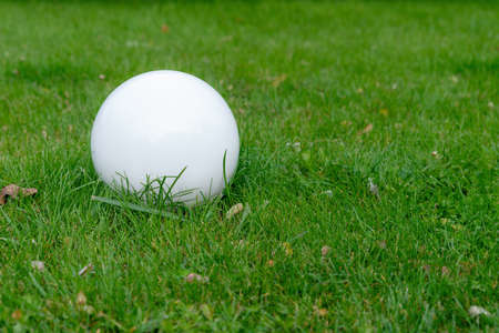 Lighting ground street lamp in the shape of a ball mounted on a green lawn in the park. Street round white lanterns. Copy space for you textの写真素材