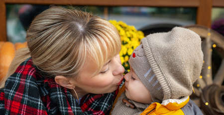 Mother having fun with her little son outdoors in autumn park. Mom kisses her little baby, close-up. Love and care. Autumn and Thanksgiving holiday party background.の写真素材