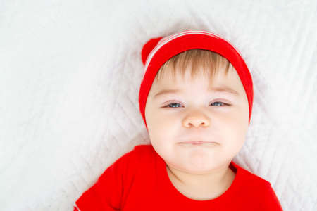 Little baby wearing Christmas clothes squints his eyes and smiles ridiculously. Close up portrait of a child with emotions on his face on a white background. Looking at camera. Winter holidaysの写真素材