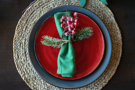 Festive christmas table setting with green napkin decorated with a sprig with berries and fir...