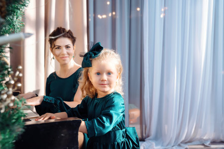 Portrait of a little girl in cute green dress playing the piano decorated with Christmas ornaments....